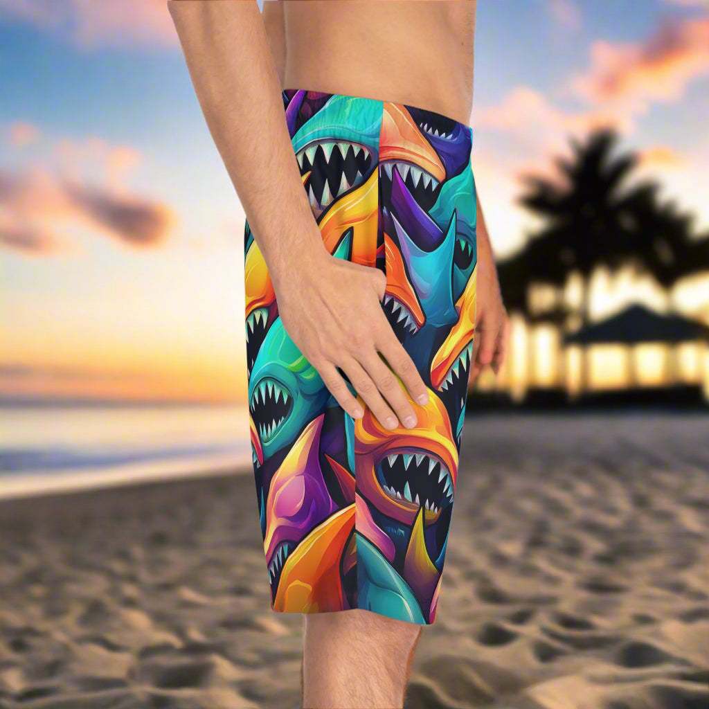 Men's board shorts with colorful surreal shark pattern worn by surfer show side view with his thumb in his pocket