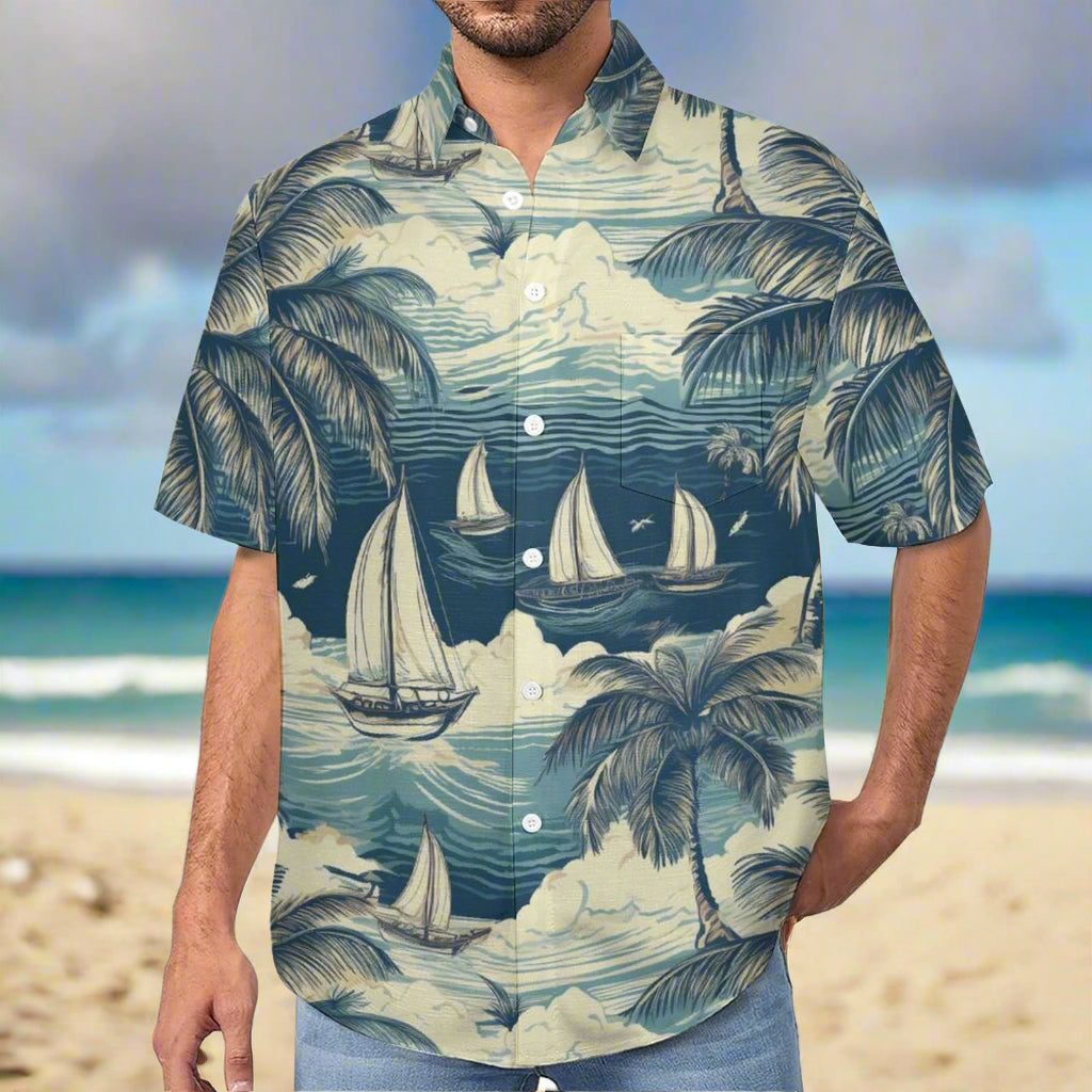 Man wearing a button up Hawaiian shirt with a teal toned graphic tropical design featuring palm trees and sailboats, standing on a beach in Hawaii