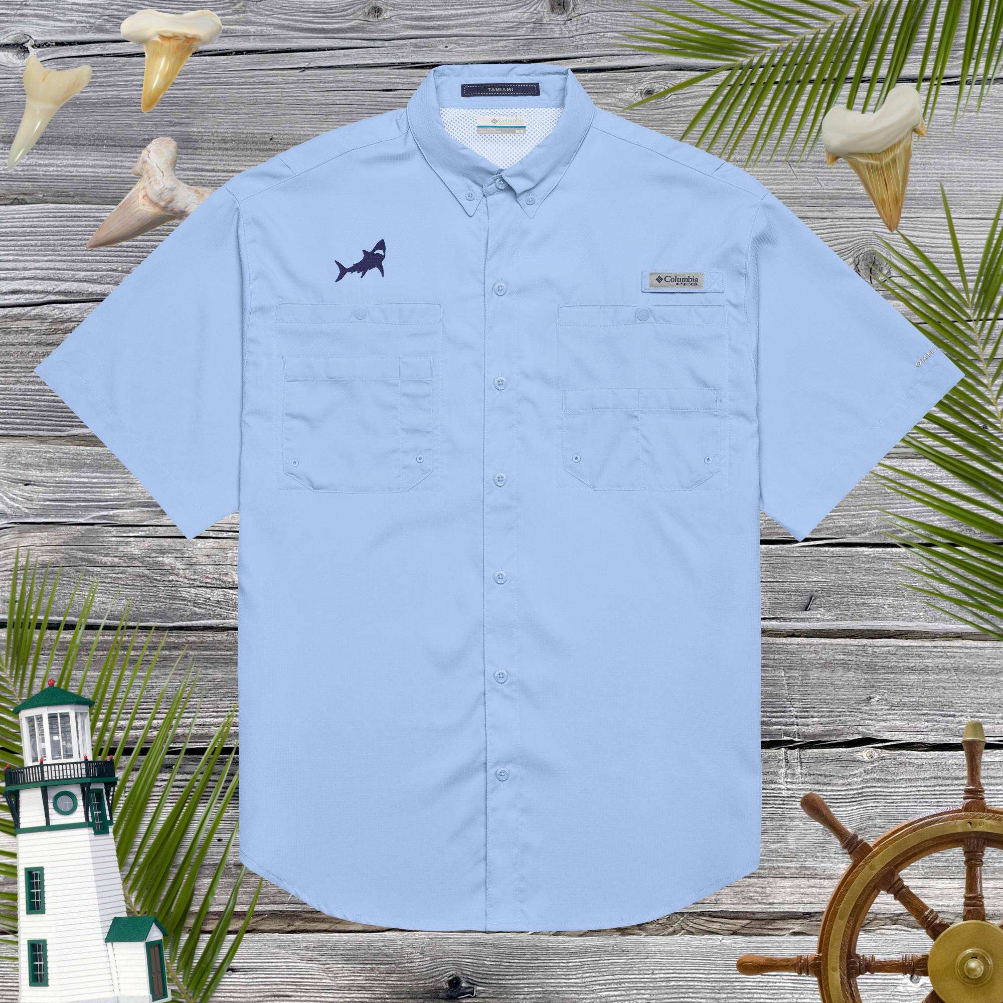 Light blue short-sleeve Columbia Fishing shirt with cool shark embroidery over a wooden background with lighthouse and palm leaves.