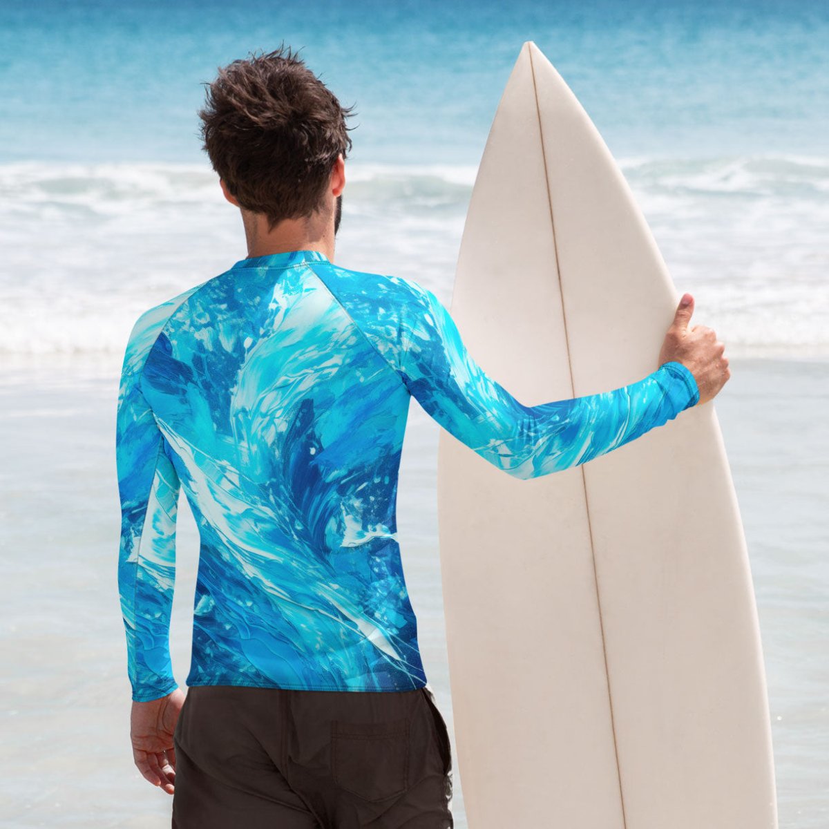 Surfer wearing a blue and white water patterned rash guard holding a surfboard on a beach