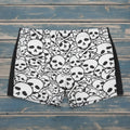 Person wearing black and white skull patterned swim shorts on a beach.