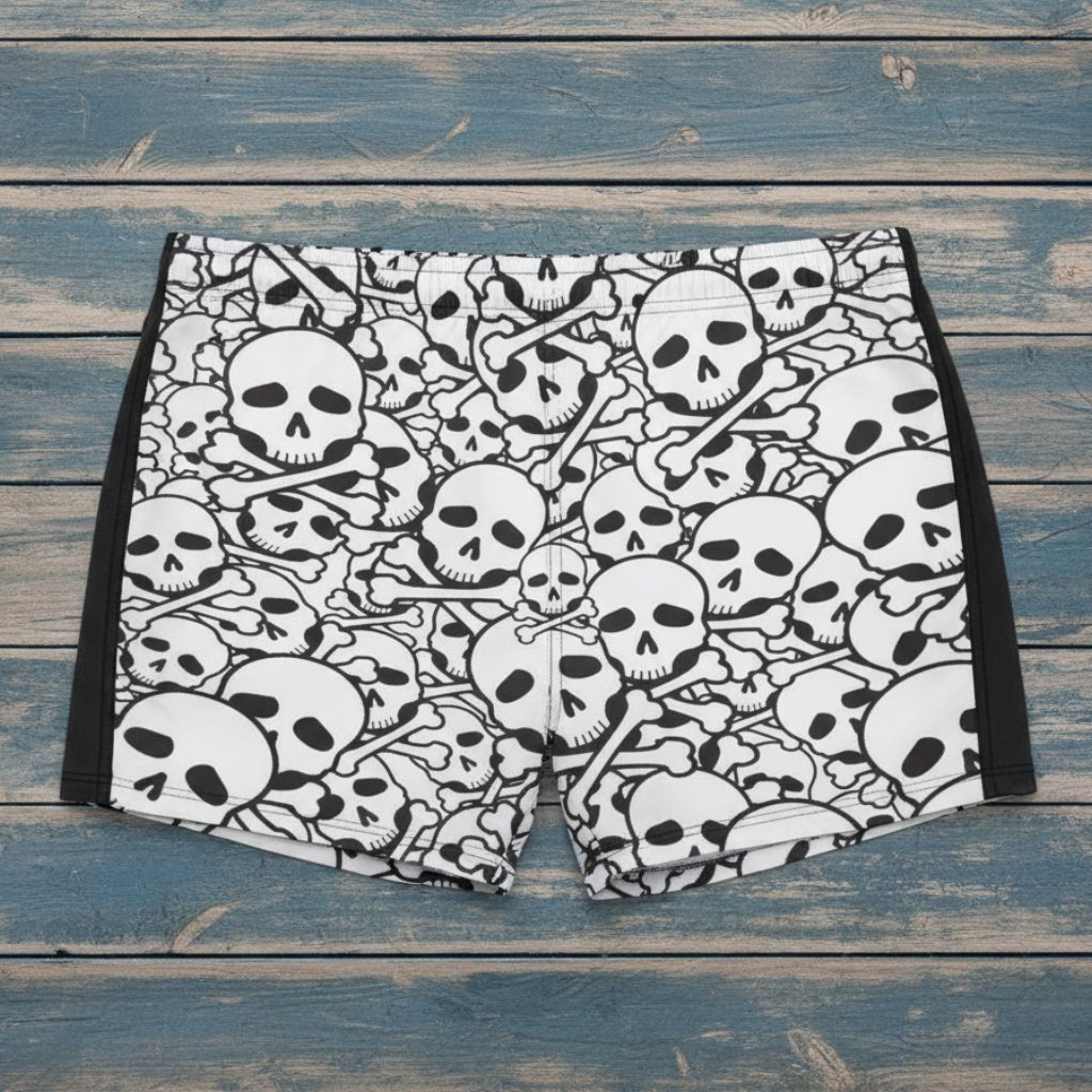 Person wearing black and white skull patterned swim shorts on a beach.