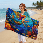 A woman on a sandy beach holds up a large beach towel featuring a colorful stained-glass style illustration of a mermaid swimming through blue water with coral and fish.