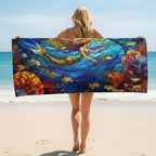 A woman on a sandy beach holds up a large Mermaid Beach Towel featuring a colorful stained-glass style underwater scene with a mermaid, blue water, and coral reef.