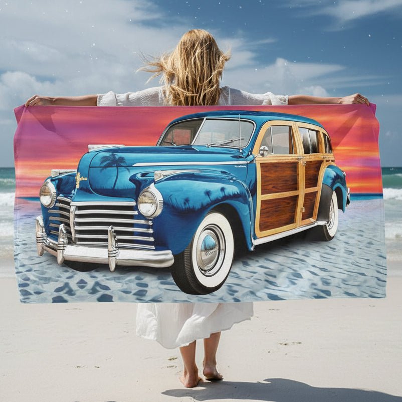 Woman on Moonlight Beach holding up a rectangular beach towel featuring a vintage blue wood-paneled station wagon on a sandy beach under a colorful sunset sky.