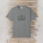 A gray short-sleeve crewneck t-shirt featuring a dark gray spiral ammonite shell graphic on the chest, displayed flat against a rustic light wood plank background.
