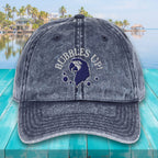 Denim cap with 'Bubbles Up!' text and parrot design on a teal surface with a waterfront background