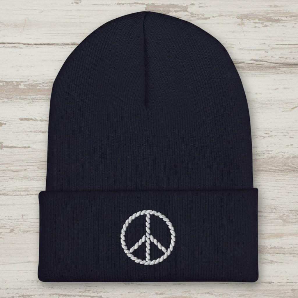 A dark navy blue ribbed knit beanie hat featuring a white embroidered peace sign on the front cuff, set against a plain white background.
