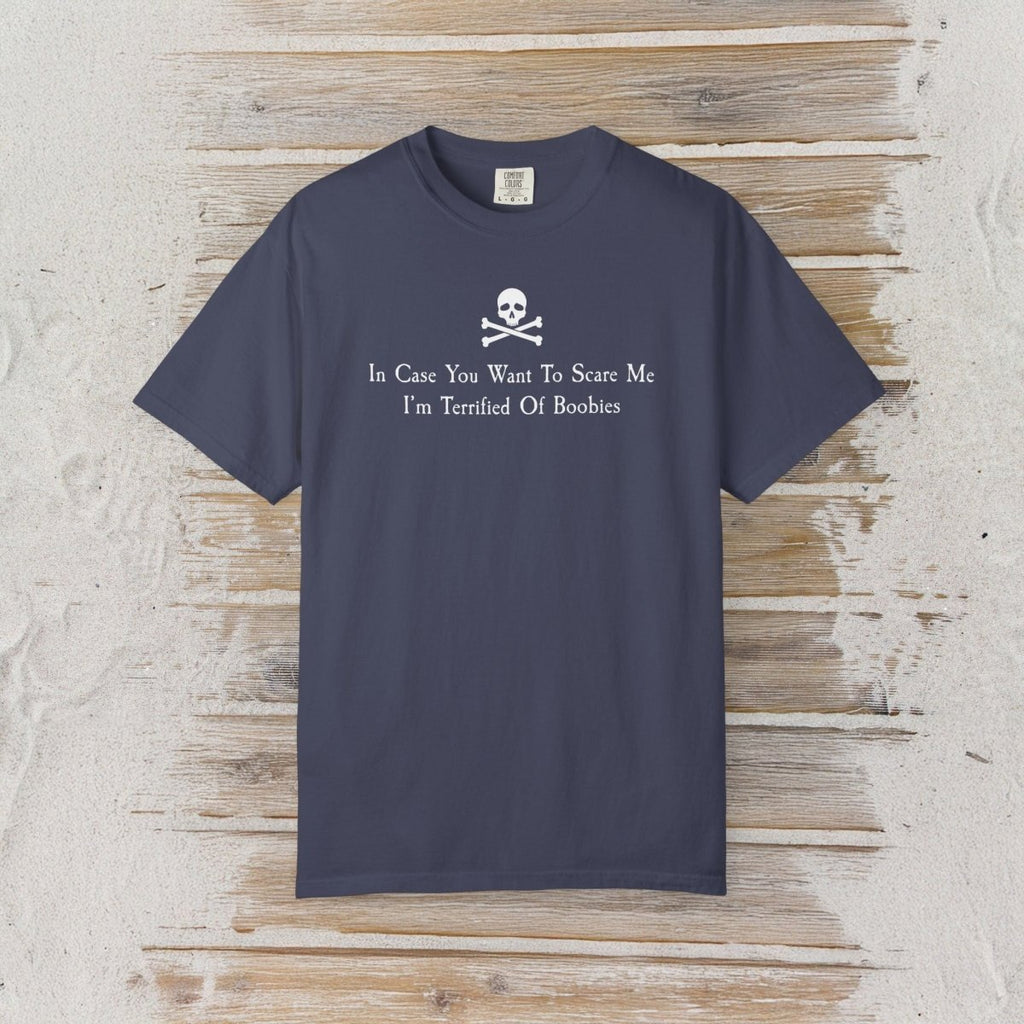 A navy blue short-sleeve t-shirt with a white skull and crossbones graphic and the text 'In Case You Want To Scare Me I'm Terrified Of Boobies' printed on the chest, displayed flat on a rustic light wood background.