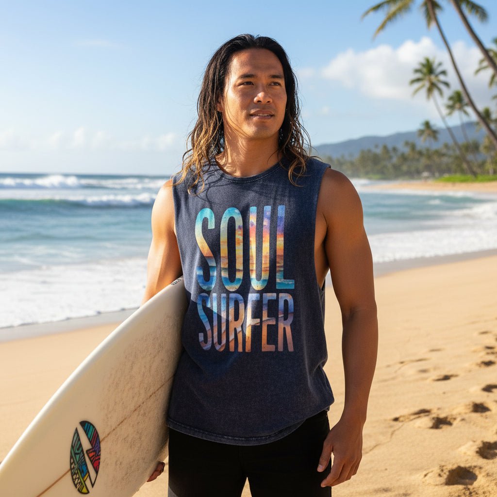 A man wearing a sleeveless dark blue-gray muscle tank top with 'SOUL SURFER' printed in a colorful gradient text design, paired with black board shorts on Hawaii's North Shore 