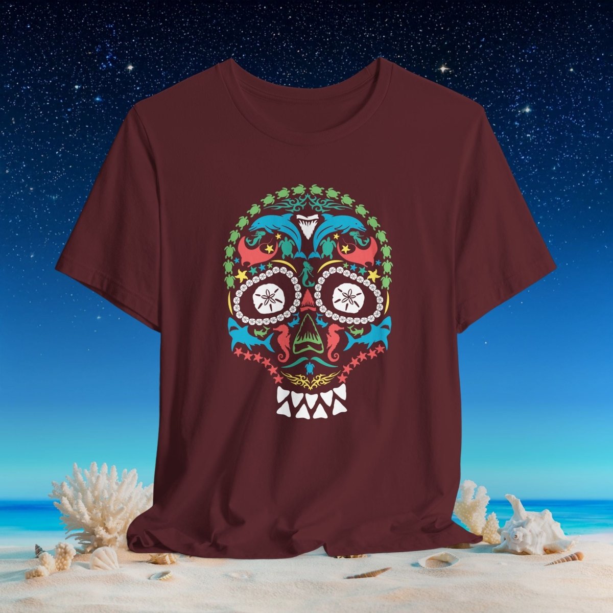 A maroon short-sleeve crewneck t-shirt featuring a colorful ocean animals sugar skull graphic on the front, set against a beach and starry night sky background.