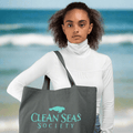 Young lady holding a black tote bag with 'Clean Seas Society' logo on Cocoa Beach