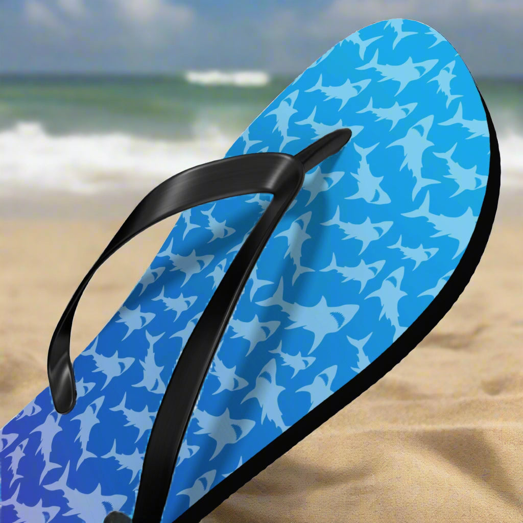 Blue ombre flip-flop with shark pattern and black strap on a beach background