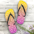 Pair of flip-flops with a gradient design on a wooden surface with flowers.