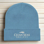 Organic Blue Beanie with Embroidered Clean Seas Society logo on a nautical wood backdrop