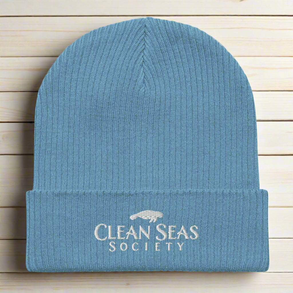 Organic Blue Beanie with Embroidered Clean Seas Society logo on a nautical wood backdrop