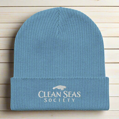 Organic Blue Beanie with Embroidered Clean Seas Society logo on a nautical wood backdrop