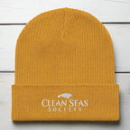 Mustard Yellow Organic Ribbed Beanie with Clean Seas Society logo on a nautical wood background