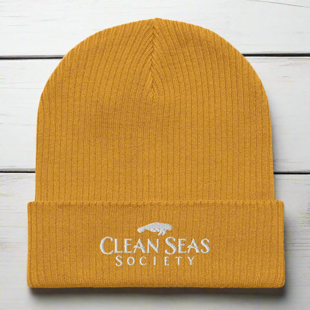 Mustard Yellow Organic Ribbed Beanie with Clean Seas Society logo on a nautical wood background