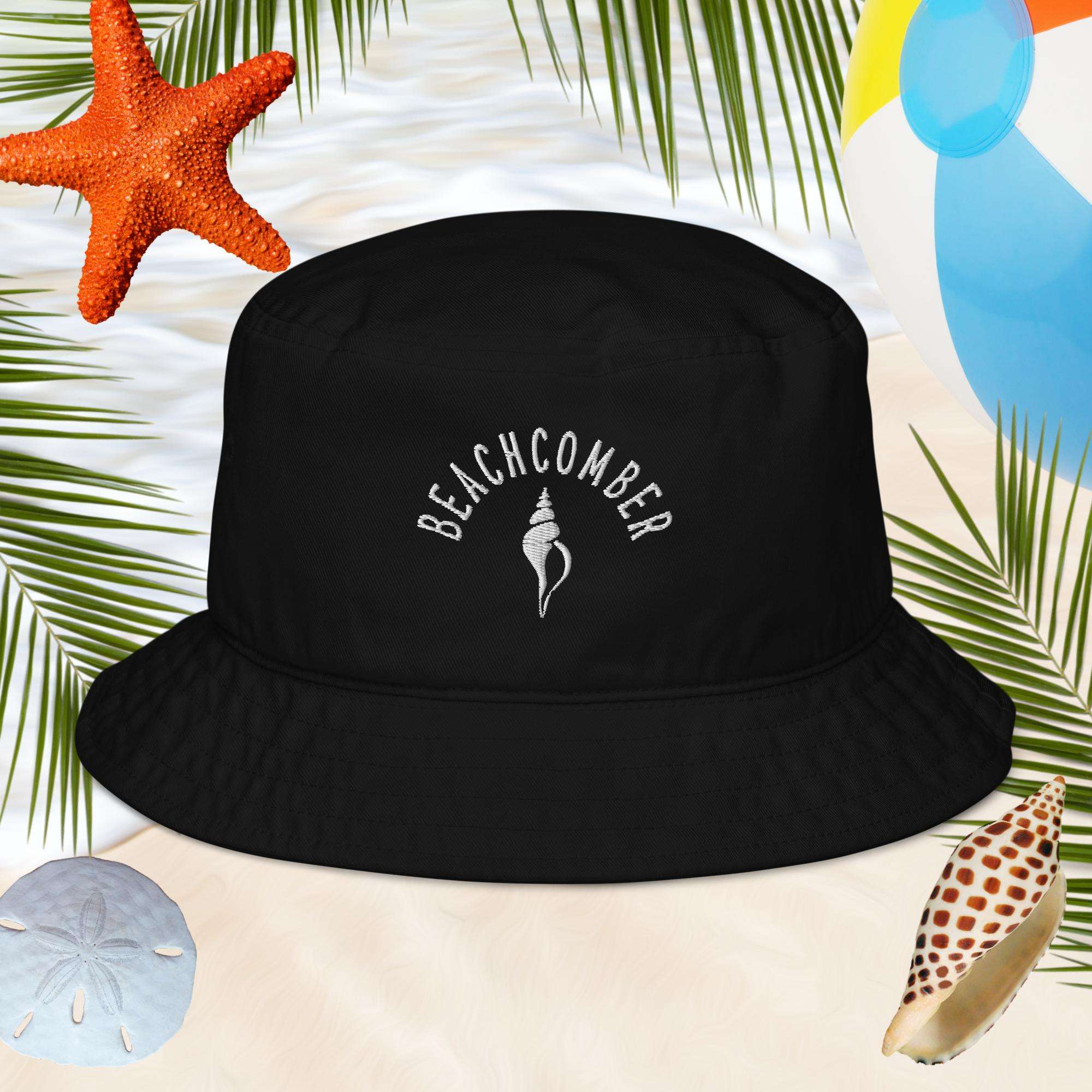 Black bucket hat with 'BEACHCOMBER' text on a sandy background with beach elements.
