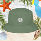 Green bucket hat with an embroidered sand dollar design on a beach-themed background with starfish, shells, and palm leaves.