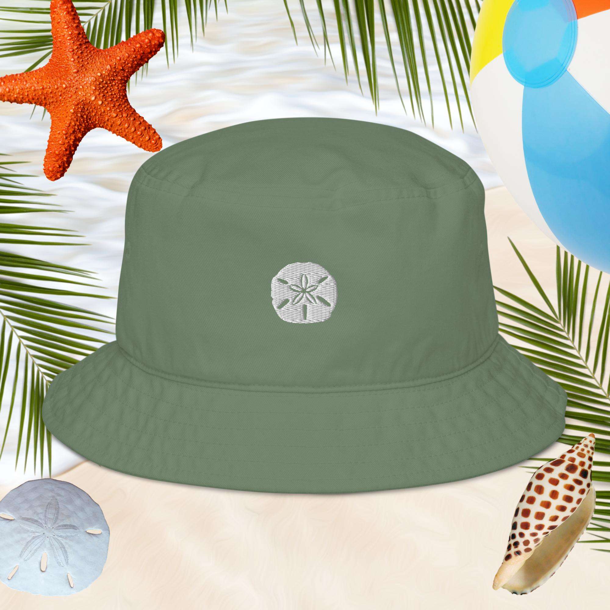 Green bucket hat with an embroidered sand dollar design on a beach-themed background with starfish, shells, and palm leaves.