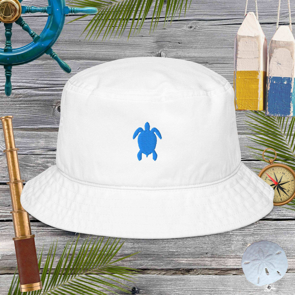 White bucket hat with blue turtle design on a wooden surface with nautical items.
