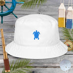 White bucket hat with blue turtle design on a wooden surface with nautical items.