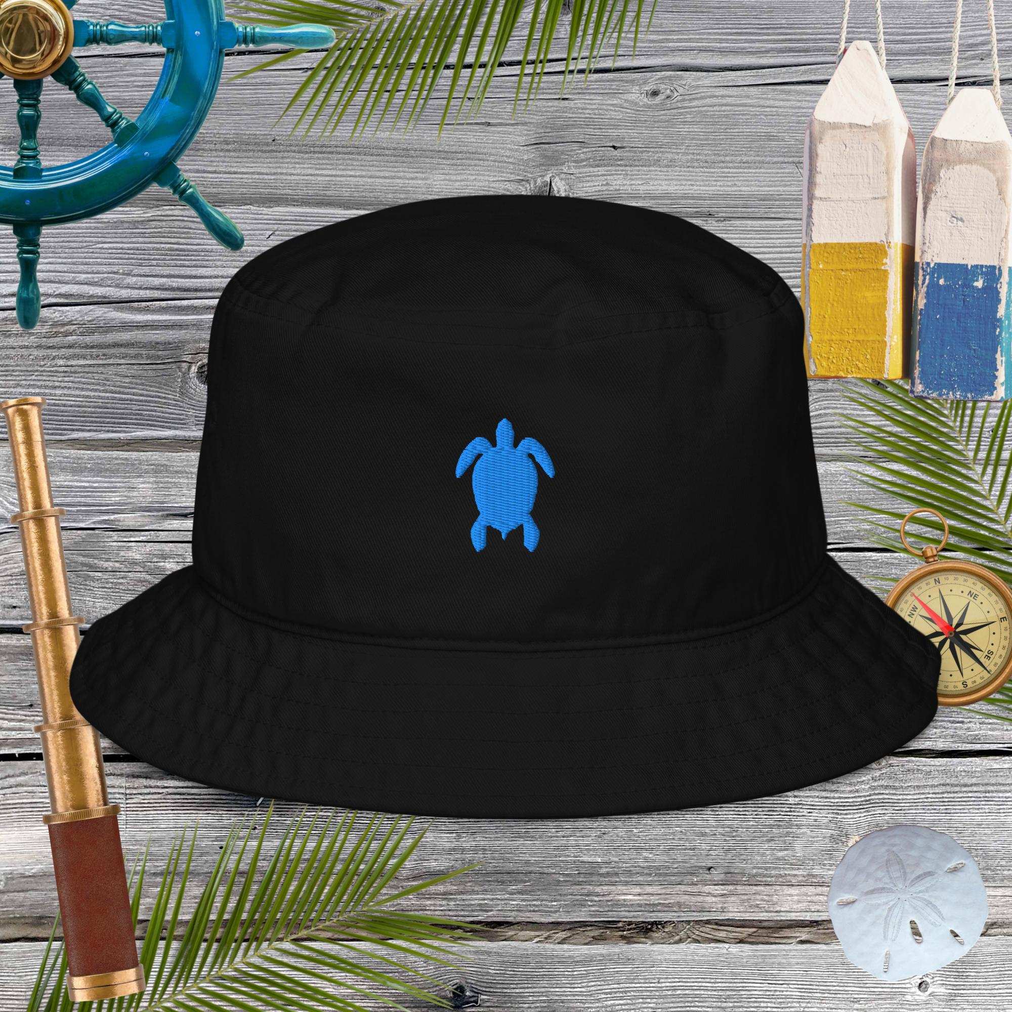 Black bucket hat with a blue turtle logo on a wooden background with nautical items.