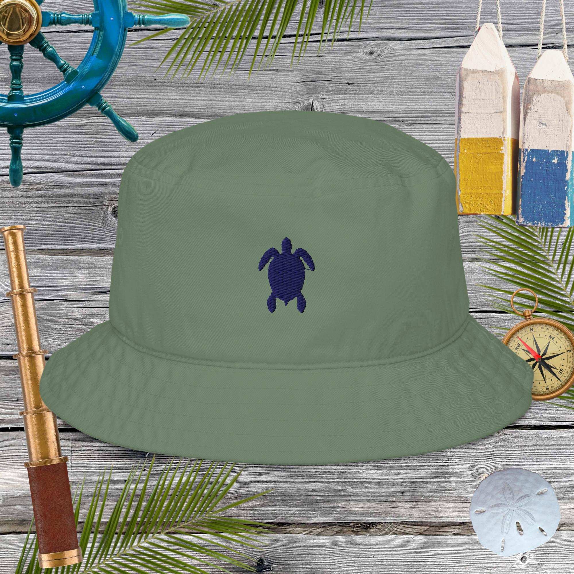 Green bucket hat with a turtle emblem on a wooden background with nautical items.