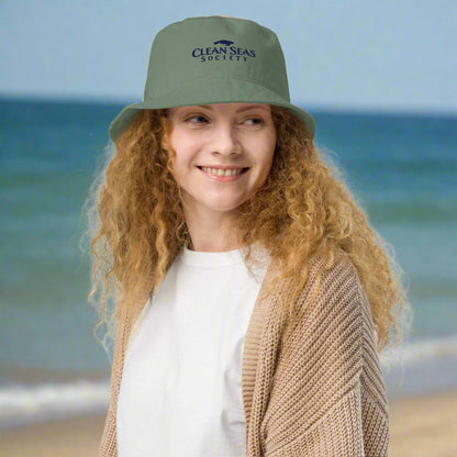 Cute Girl wearing an Organic Bucket Hat with Clean Seas Society logo standing on beach and smiling because it's clean
