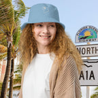 Woman wearing a blue Parrot Head bucket hat with palm trees and a scenic highway sign in the background