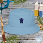 Blue bucket hat with a turtle emblem on a wooden background with nautical items.