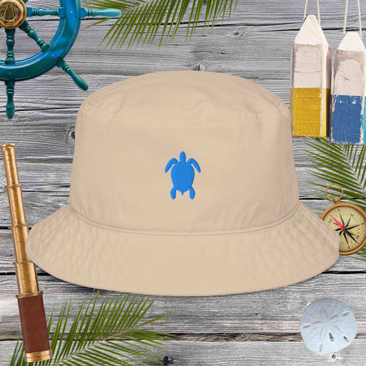 Beige bucket hat with blue turtle design on a wooden surface with nautical items.