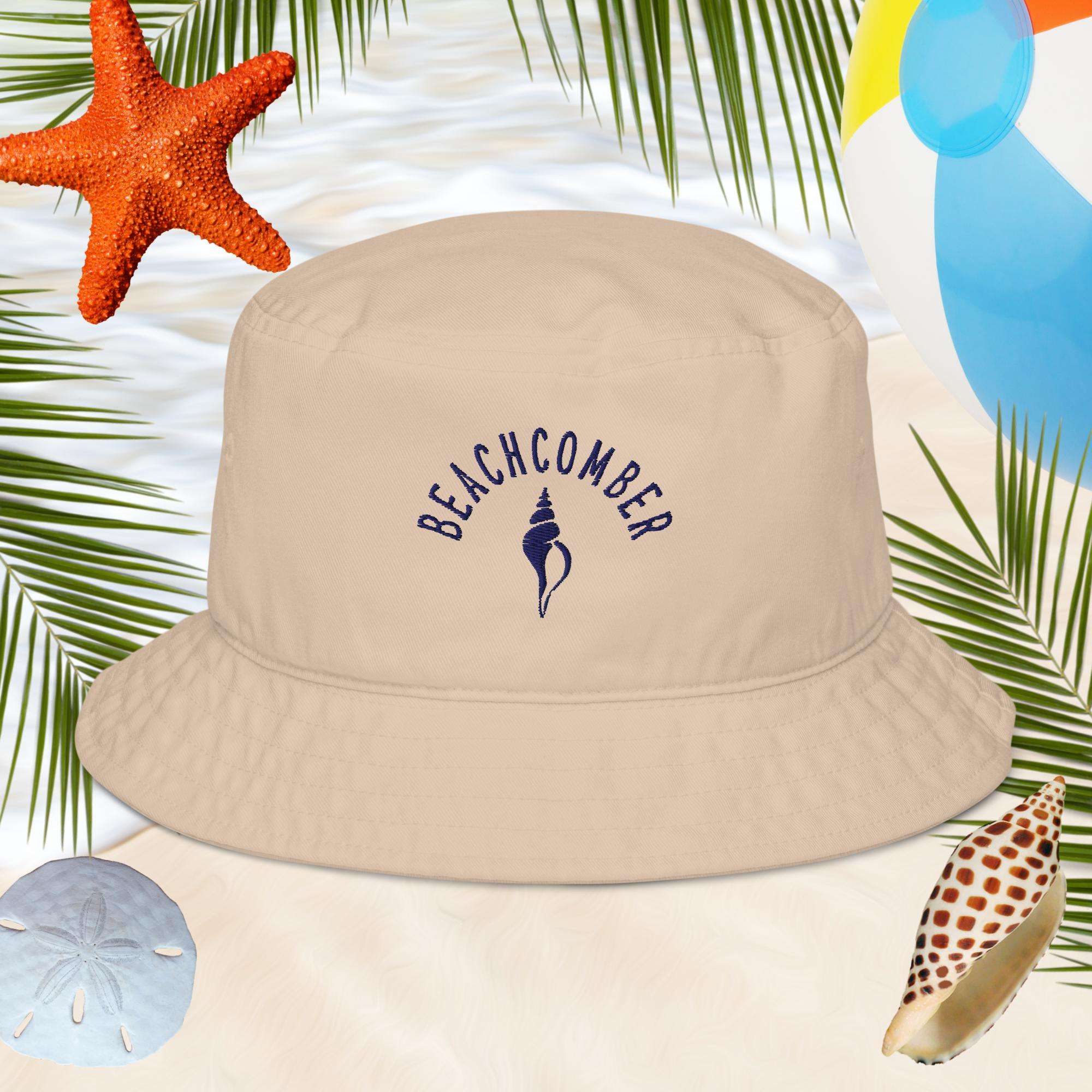 Beige bucket hat with 'BEACHCOMBER' text and shell design on a beach-themed background with starfish, shells, and palm leaves.