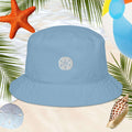 Blue cotton bucket hat with a sand dollar design on a beach-themed background with palm leaves, starfish, and shells.