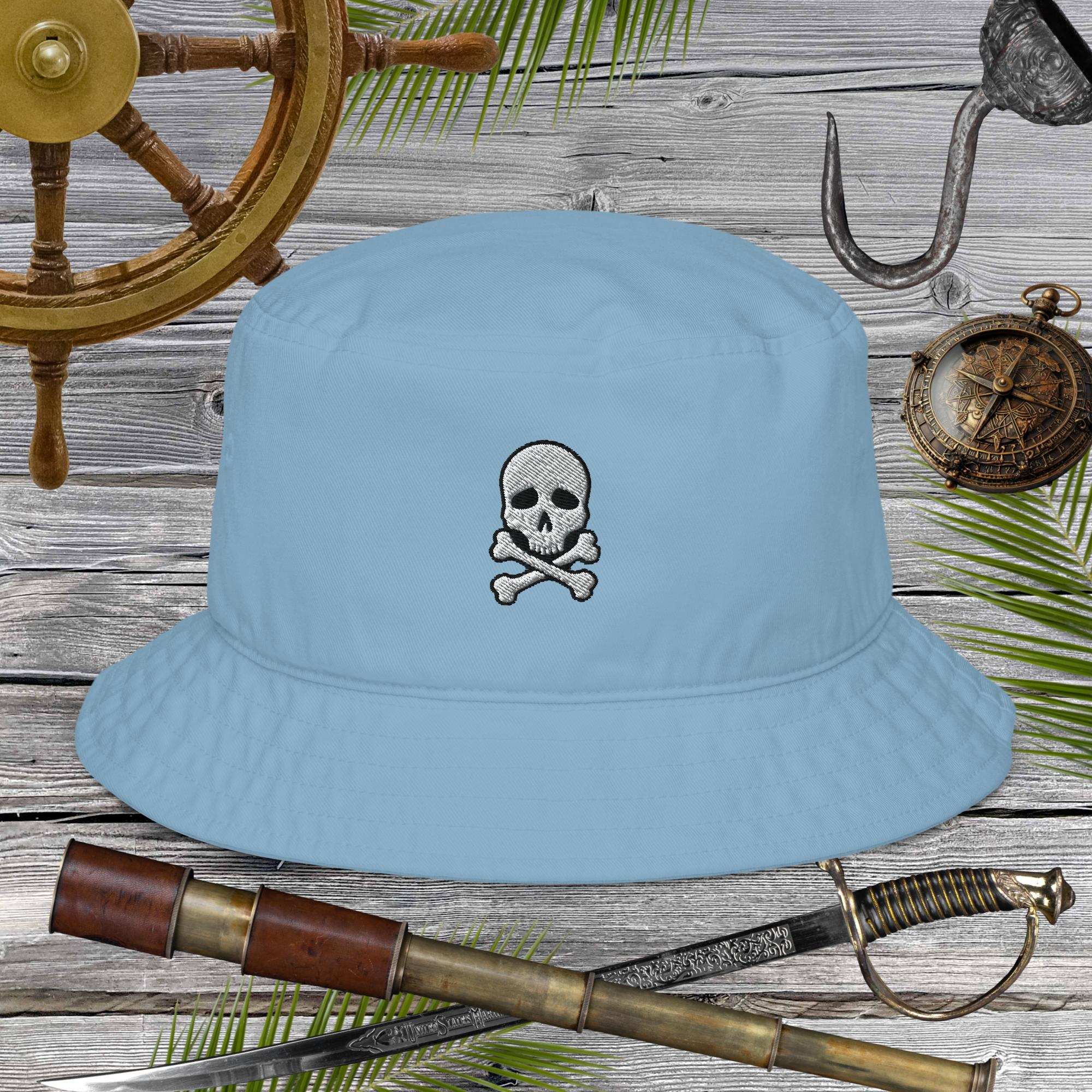 Light blue bucket hat with skull and crossbones design on a wooden background with pirate-themed items.