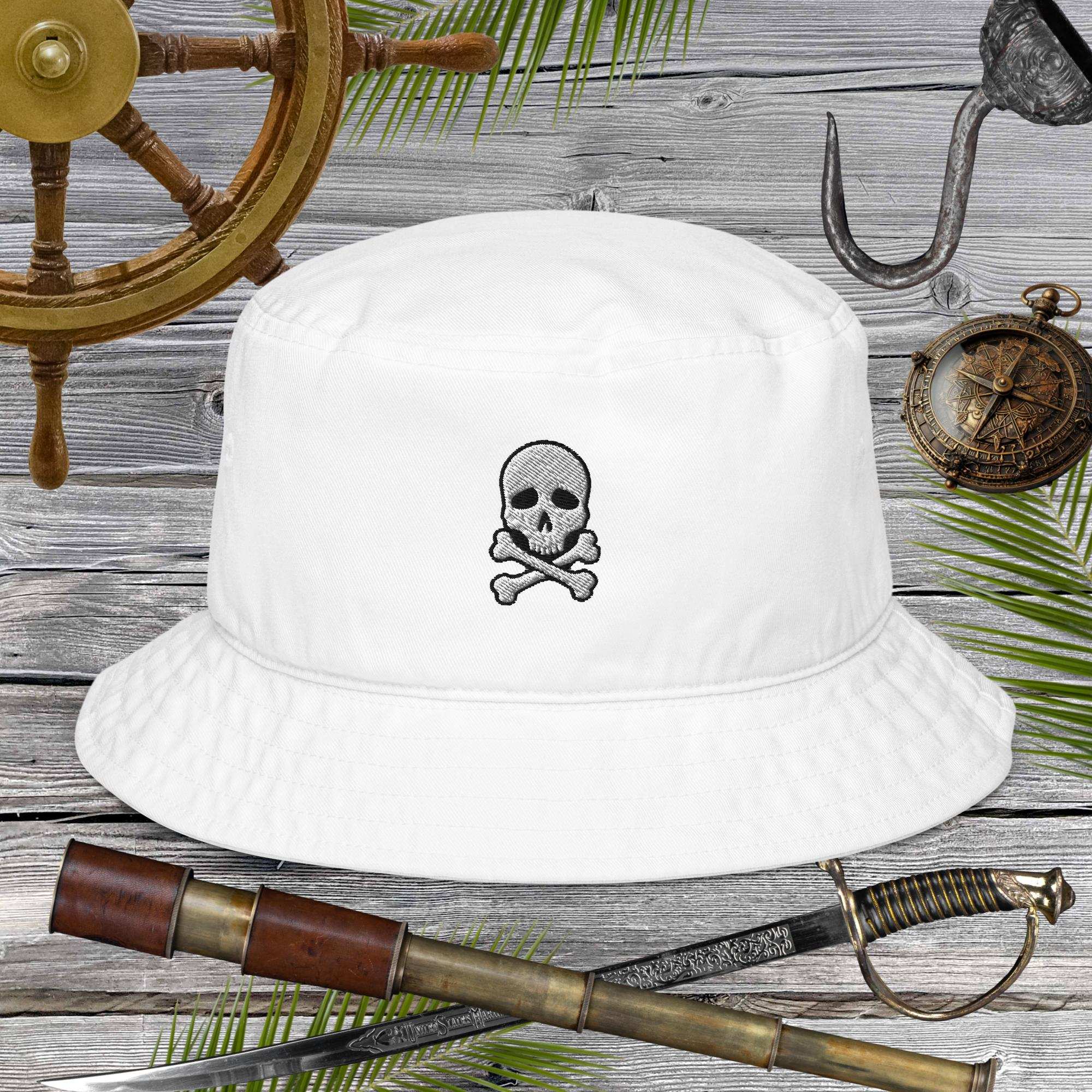 White bucket hat with skull and crossbones design on a wooden background with pirate-themed items.