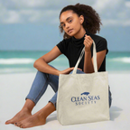 girl holding a tote bag with 'Clean Seas Society' logo on a white sandy beach