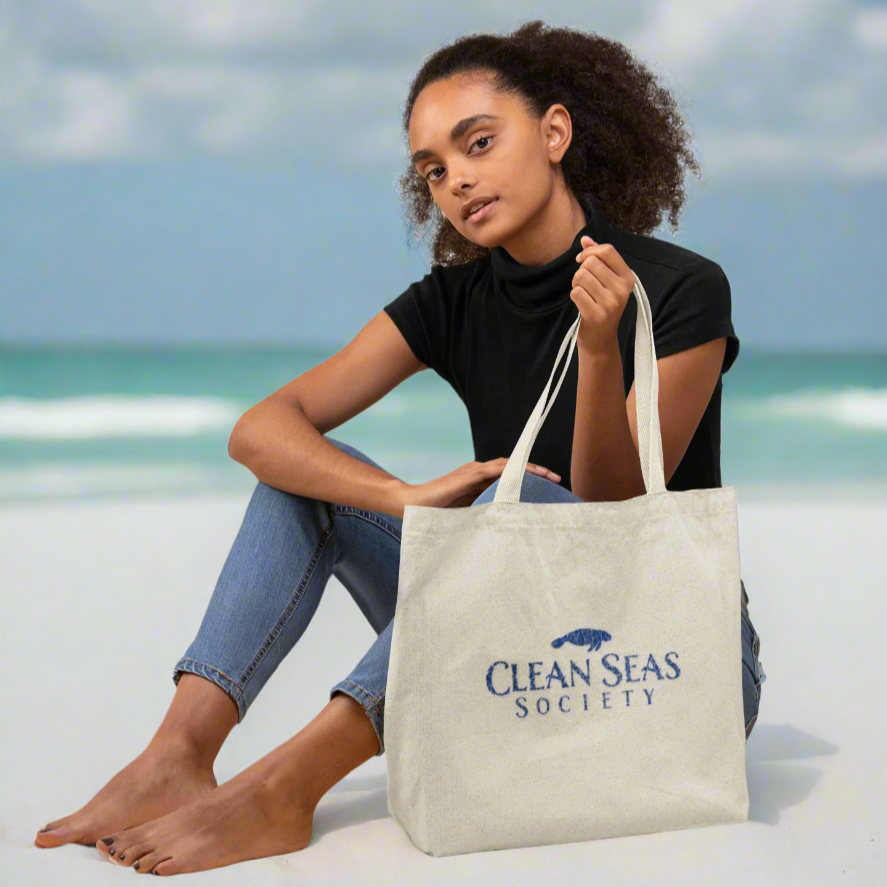 girl holding a tote bag with 'Clean Seas Society' logo on a white sandy beach
