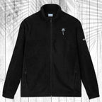 A black fleece zip-up jacket with a stand collar, shown flat against a white wood plank background with a palm leaf pattern overlay. The jacket features a small grey palm tree embroidered on the left chest and a small  Columbia logo on the right sleeve.