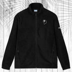 A dark gray fleece zip-up jacket with a stand collar, shown flat against a white wood plank background with a palm leaf pattern overlay. The jacket features a small white circular logo on the left chest and a small white logo on the right sleeve.