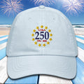 Light blue cap with 'USA 250' design on a beach with fireworks background