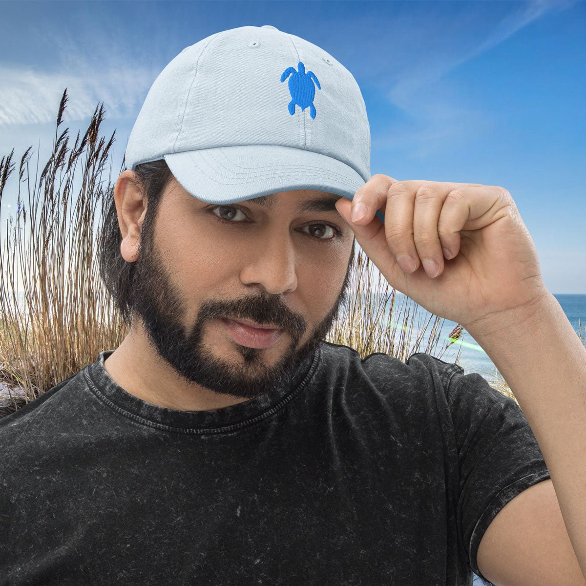Man wearing a light blue Sea Turtle Baseball Hat with a turtle logo against a beach background