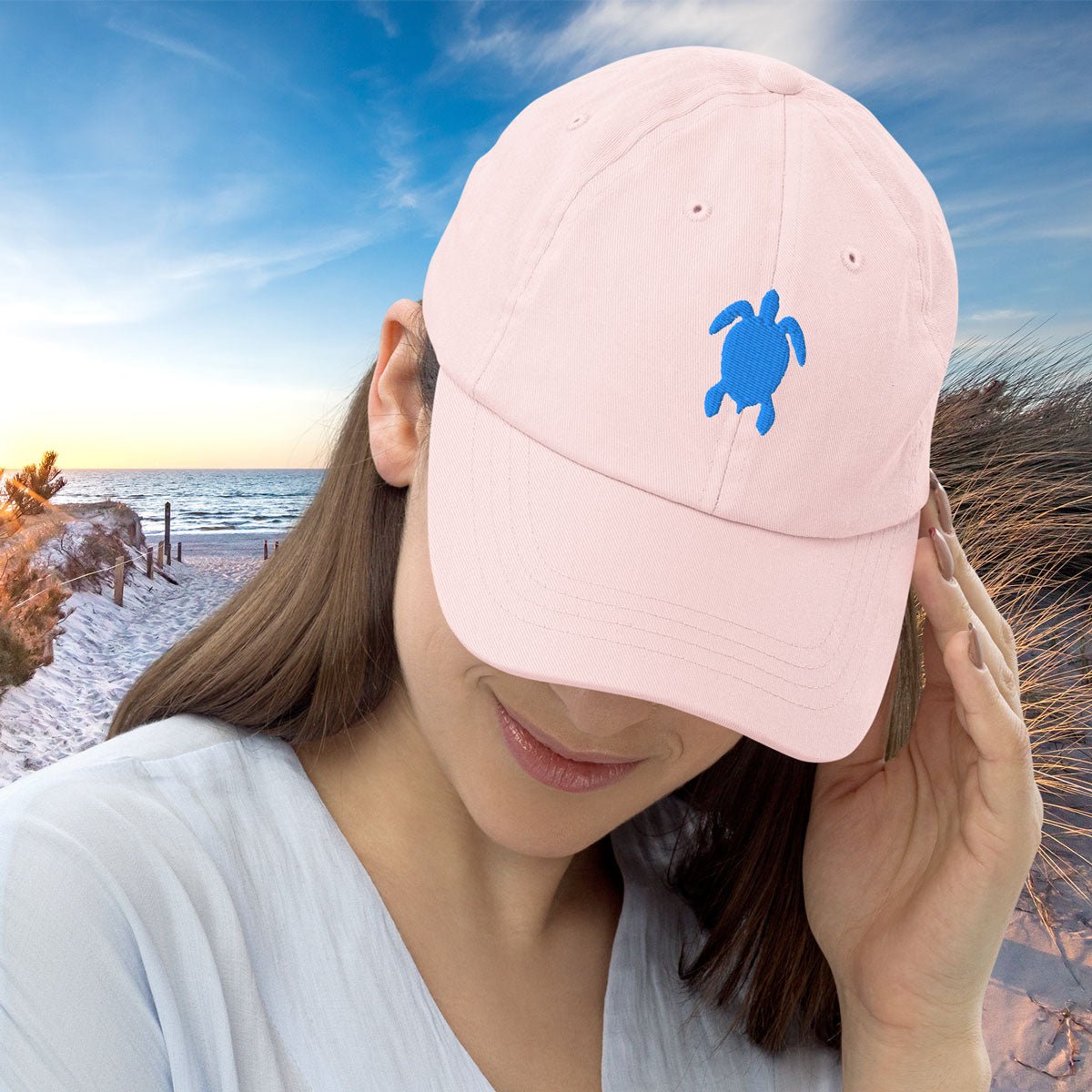 Person wearing a pastel pink cap with a blue turtle design on a beach at sunset