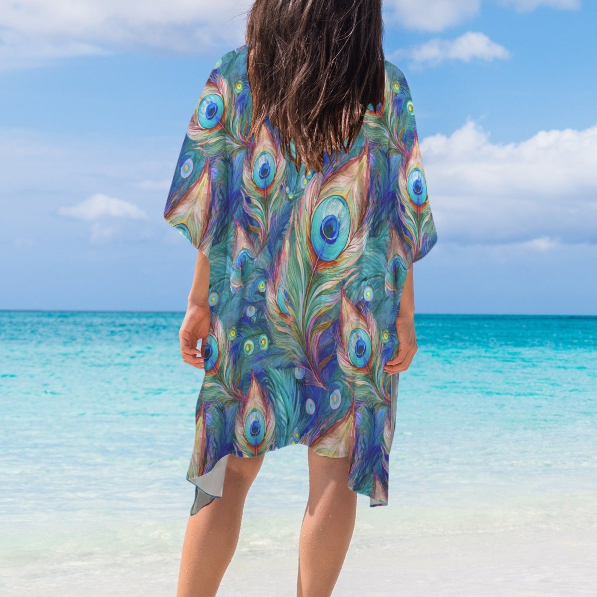 Person wearing a colorful peacock feather patterned cover-up on a beach.