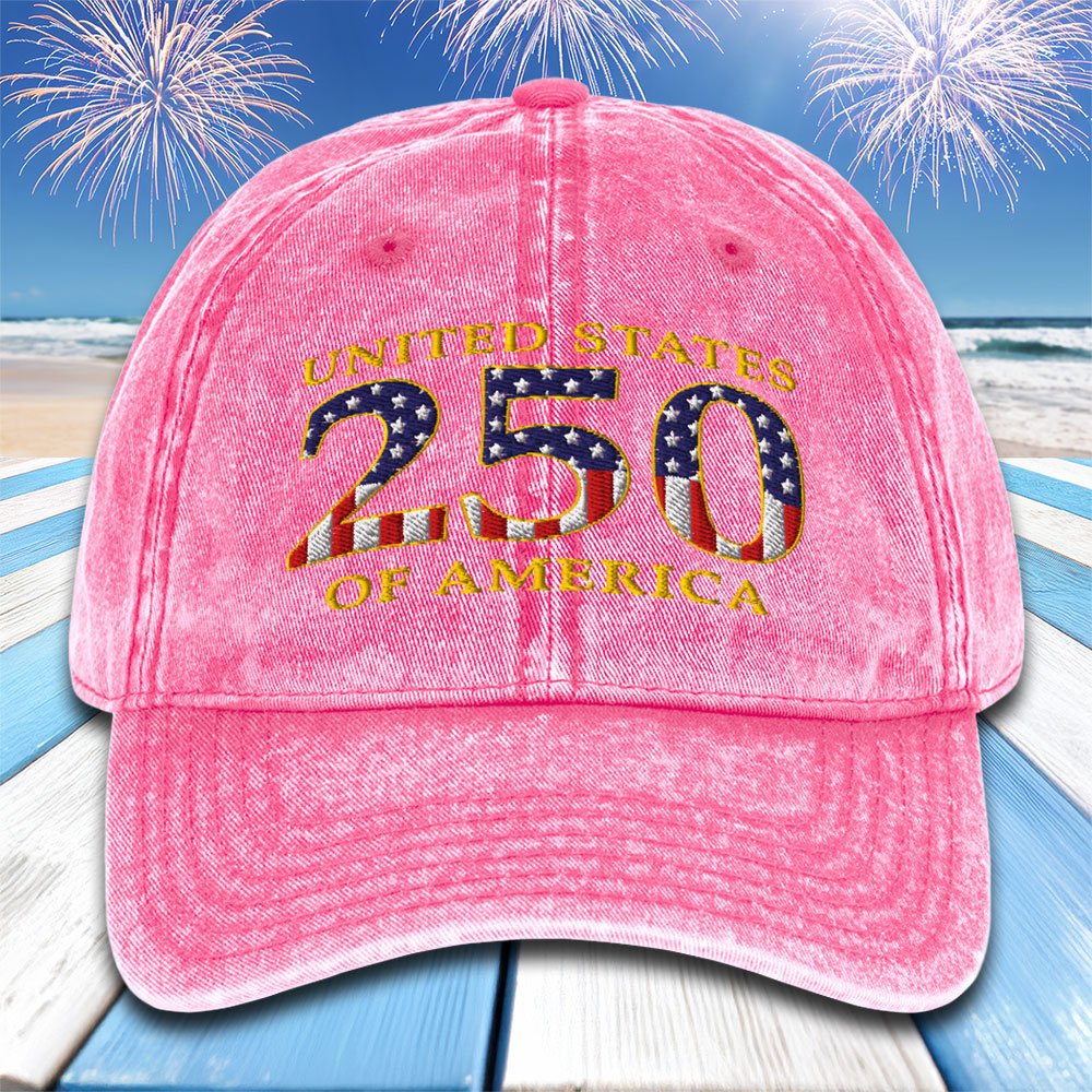 Pink cap with 'United States 250 of America' text and American flag design on a beach with fireworks background.