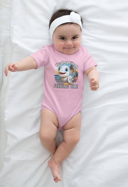 Baby wearing a pink onesie with a cartoon baby shark and feeding time text on a white blanket