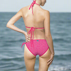 Sexy women in a bikini with pink dolphin pattern print stands on the beach and looks out over the ocean
