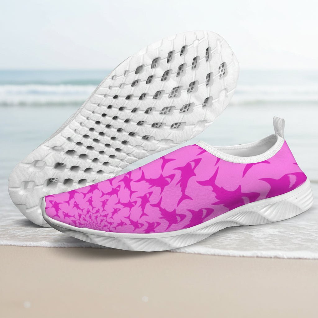 A pair of slip-on water shoes with a vibrant pink and magenta abstract pattern on the uppers and white soles, shown against a faded beach background.